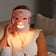 Person wearing a LED face mask with red light on a neutral background