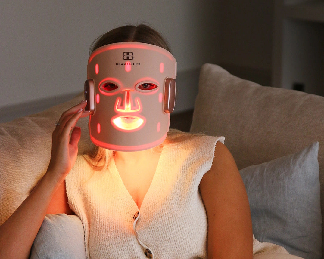 Person wearing a LED face mask with red light on a neutral background