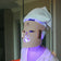 Person wearing a LED face mask with a towel on their head in a room setting.